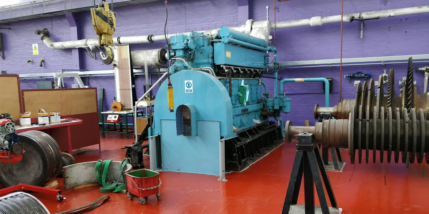Un gran motor industrial se encuentra en un taller sobre un suelo rojo.